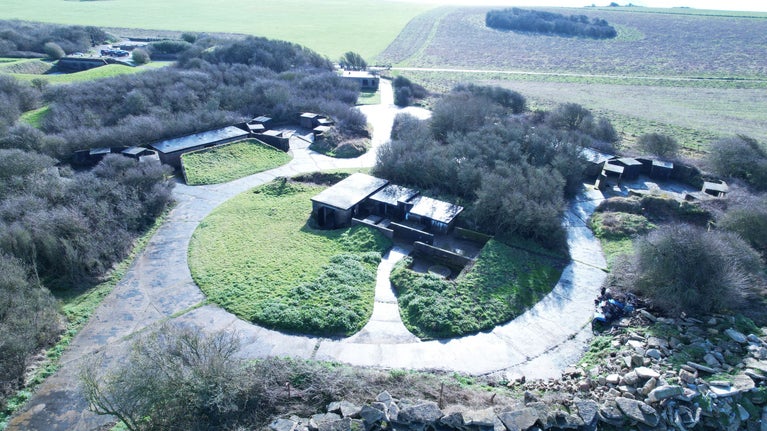 An image of a network of roads and buildings forming the semi-circular D2 Heavy Anti-Aircraft Battery. There is a series of buildings in the centre of the image, which was the command post. The circular parade ground can be seen along with another building, which was the gatehouse or gun store. The three emplacements, with their associated magazines and are clustered around the command post.